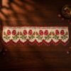 Top-down view of a traditional Parsi toran with embroidered red roses and a red and white beaded fringe, displayed on a dark wooden table with scattered rose petals and a brass bowl.