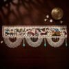 Top-down view of an intricate Parsi toran with embroidered scenes of people, horse-drawn carriages, and houses. It is finished with wide, semi-circular white beadwork and hanging turquoise beads, styled on a dark wood table with a brass incense burner.