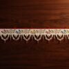 Top-down view of a white Parsi toran resting on a dark wood surface. The design features a continuous vine with pairs of multi-colored embroidered birds and a bottom fringe of white beaded scallops with hanging red beads.