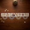 A flat top-down view of a handcrafted Parsi toran resting on a dark wood surface. The white band is embroidered with golden and maroon Zoroastrian motifs, finished with four elaborate white beaded scallops and styled with a brass incense burner and jasmine flowers.