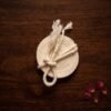 Top-down view of a sacred Kusti cord coiled into a disc on a dark wood surface, featuring a knot and tasseled ends, accented by scattered red rose petals