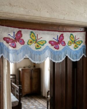 A handcrafted beaded toran with pink and yellow butterfly patterns hangs over a wooden doorframe, welcoming guests into a traditional Parsi home interior with vintage furniture.