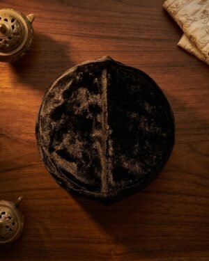 Top-down view of a black velvet Parsi topi on a wooden table with brass incense burners.