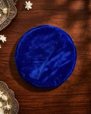 Top-down view of a royal blue velvet Parsi topi on a wooden surface with jasmine flowers.