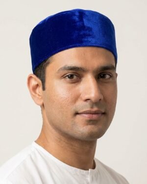Studio headshot of a man wearing a structured royal blue velvet Parsi topi, set against a plain off-white background.
