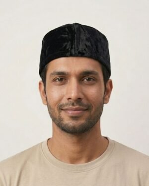 Studio portrait of a man wearing a black velvet Parsi topi and a beige t-shirt.