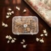 Top-down view of a box of Parsi floating wicks on a wooden surface surrounded by fresh jasmine flowers.