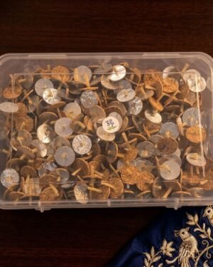 Top-down view of a transparent box packed with circular cork wicks used for Zoroastrian prayer lamps, shown against a dark wood and blue embroidered fabric background