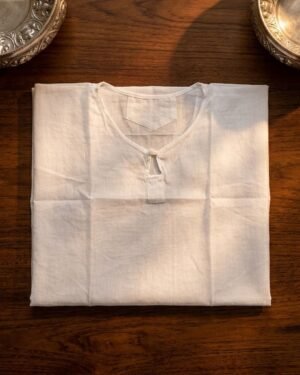 A folded white cotton Sudreh, a sacred Zoroastrian undershirt, placed on a dark wooden table between two ornate silver bowls.