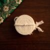 Top-down view of a coiled white wool Kusti on a dark wood table next to green floral embroidery.