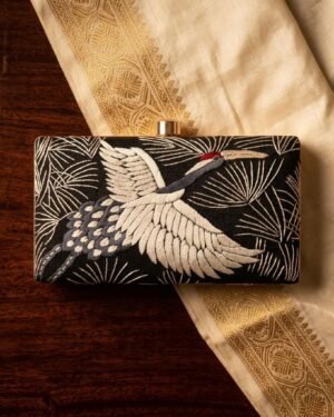 A blue rectangular clutch with white crane embroidery resting on a cream and gold silk sari