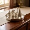 A silver Parsi ceremonial tray on a wooden sideboard in a naturally lit home.