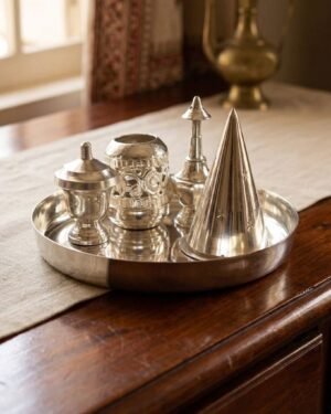 A silver Parsi ceremonial tray on a wooden sideboard in a naturally lit home.