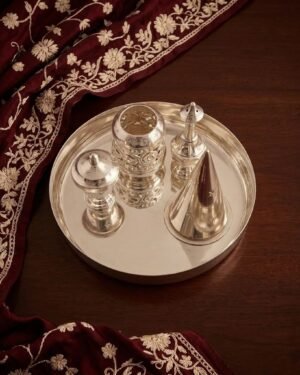 A polished silver Parsi Sese set on a wooden table, styled with a maroon embroidered fabric.