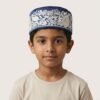 A portrait of a young boy wearing a blue embroidered Parsi topi and a plain white t-shirt