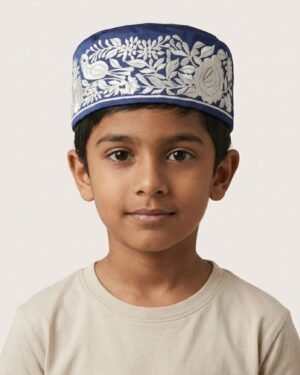 A portrait of a young boy wearing a blue embroidered Parsi topi and a plain white t-shirt