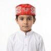 A young boy wearing a white shirt and a red embroidered Parsi topi.