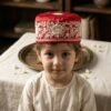 A young boy wearing a traditional red embroidered Parsi topi and a white kurta.