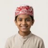 Studio portrait of a smiling young boy wearing a white Parsi prayer cap adorned with intricate red bird and floral Gara embroidery, set against a neutral background.