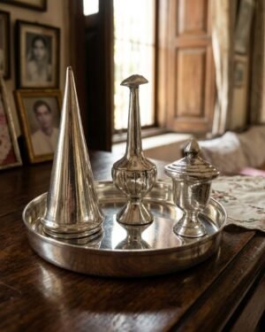 A traditional Parsi silver Sesklo(sase) set on a tray, featuring a pigani (rosewater sprinkler), a gulabpas (cone-shaped container), and a kankavati (small urn)."
